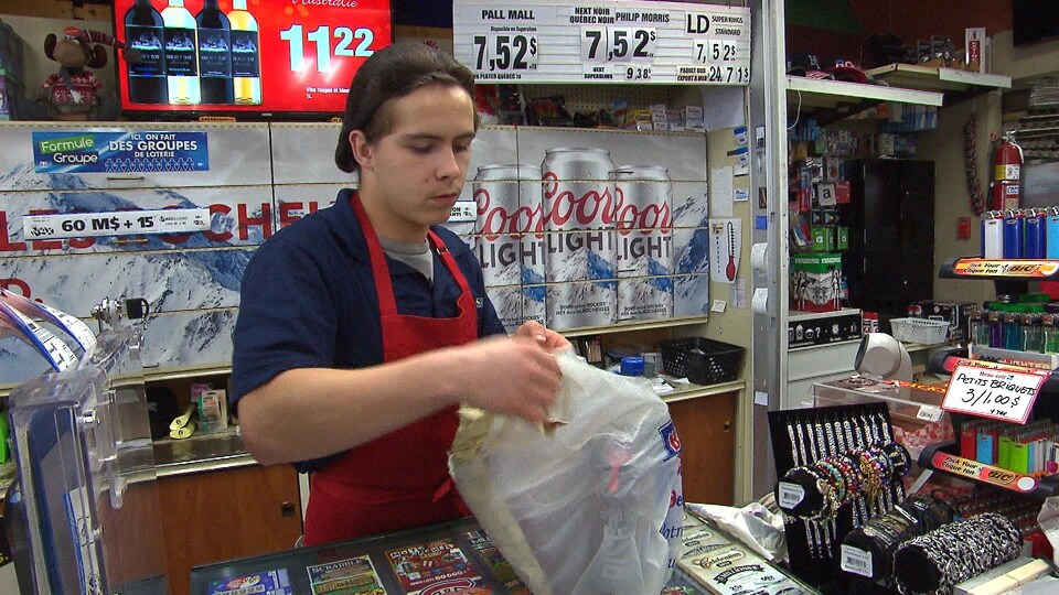 Un employé place les achats d'un client dans un sac de plastique.