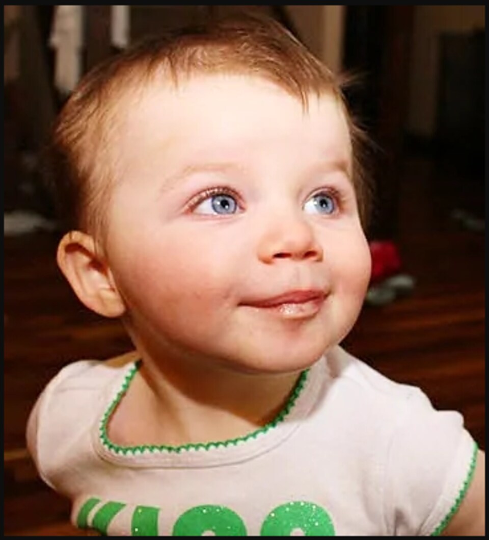 Mackenzy Woolfsmith, 11 mois, affiche de grands yeux gris et alors qu'elle regarde vers la droite, sourire en coin.