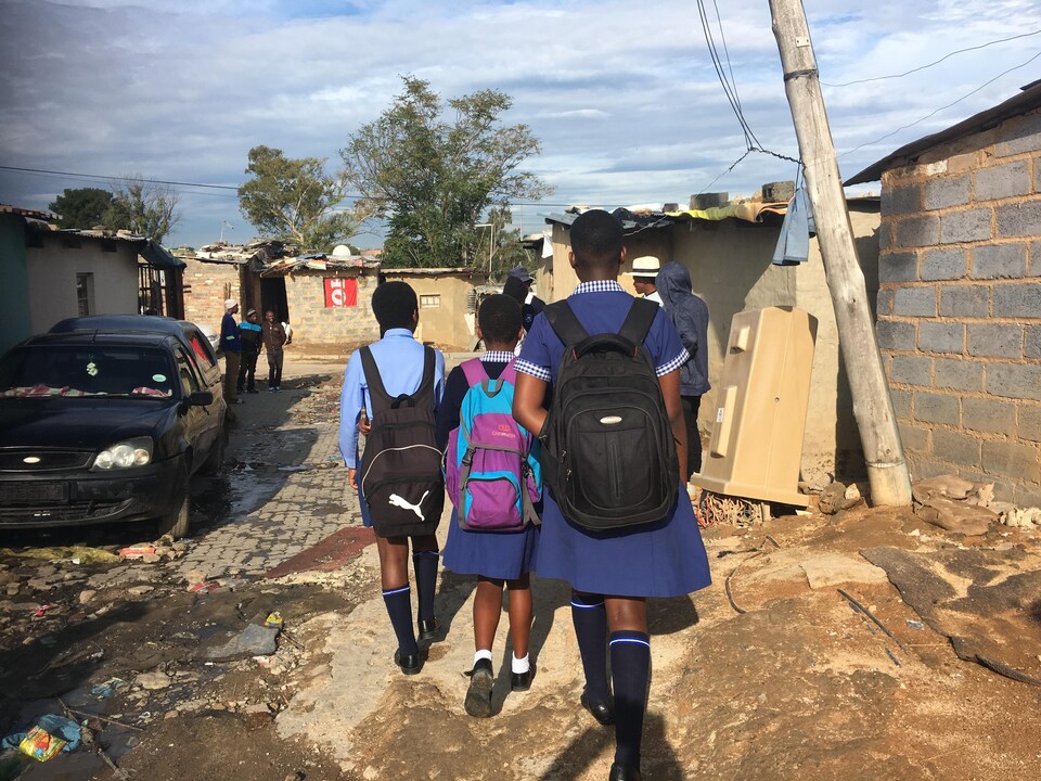 Des enfants en uniforme et avec un sac à dos marchent dans la rue.