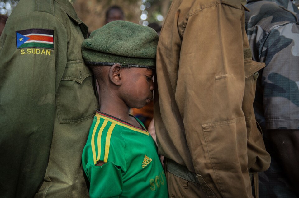 Un enfant-soldat récemment libéré est en rang entre deux adultes.