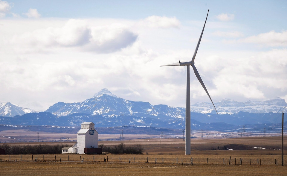 Paysage du sud de l'Alberta avec une éolienne en premier plan à côté d'un ascenseur à grain et les montagnes Rocheuses en arrière-plan