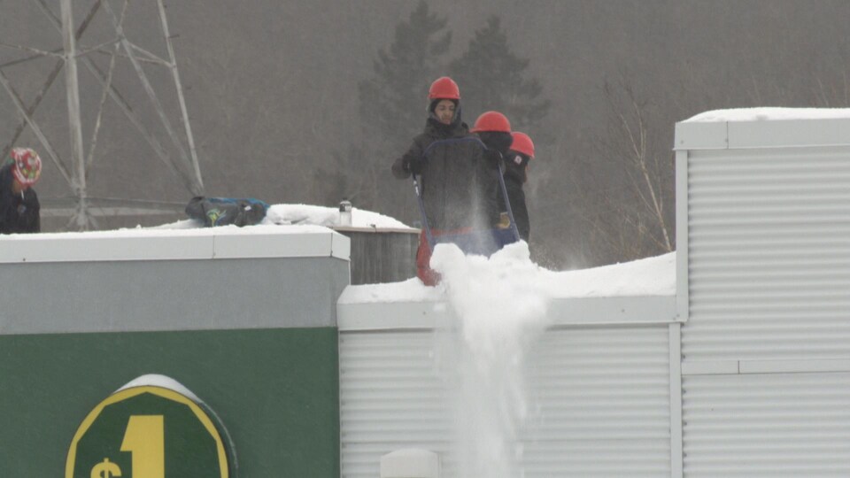 Un travailleur pousse la neige en bas du toit à l'aide d'une pelle.