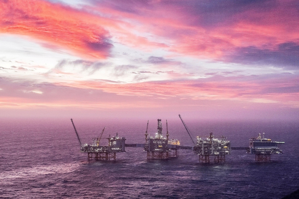 Des plateformes pétrolières en mer sous un ciel rose et mauve.