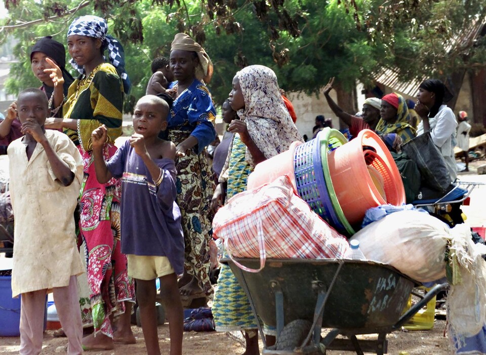 Des femmes et des enfants se tiennent près de leurs biens après avoir été évacués de leur village en raison de violences interethniques à Yelwa au Nigeria, le 4 mai 2004.