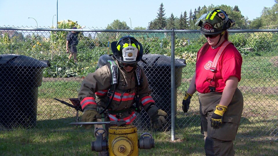 Un pompier tourne la valve de la borne avec une pince tandis qu'un autre pompier vérifie le travail.