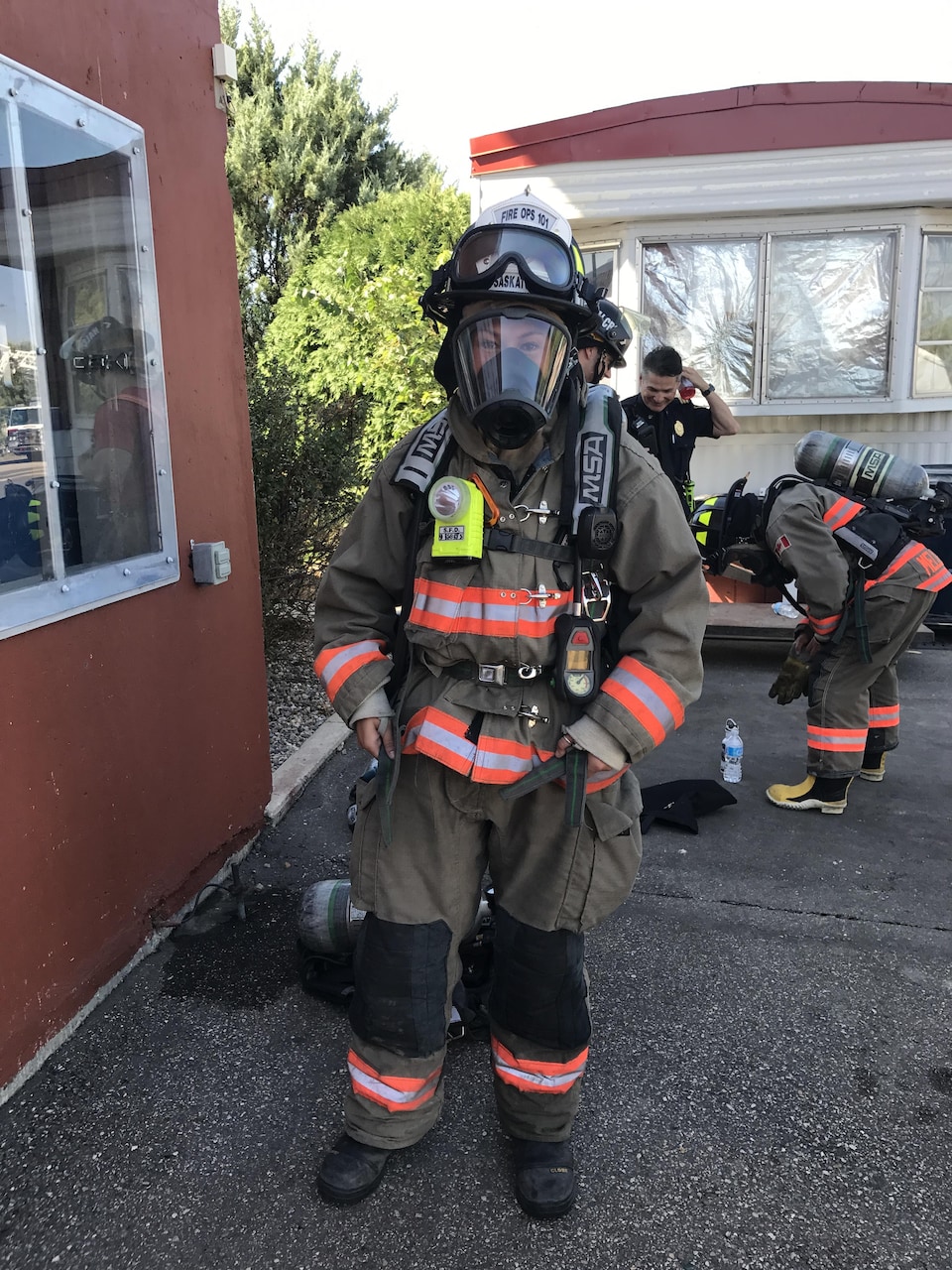 Une personne porte l'équipement de protection d'un pompier. Bottes, pantalons, manteau, casque, masque à oxygène.