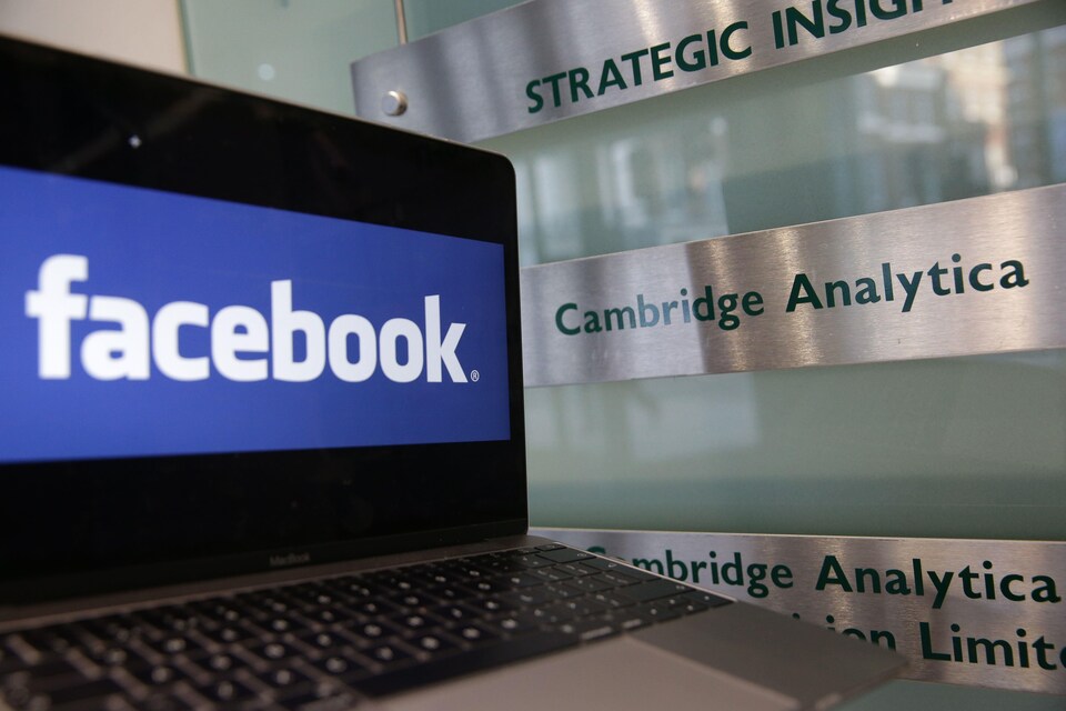 Un ordinateur portable montrant le logo de Facebook est posé à côté d'une plaque indiquant les bureaux de Cambridge Analytica, à Londres, le 21 mars 2018.