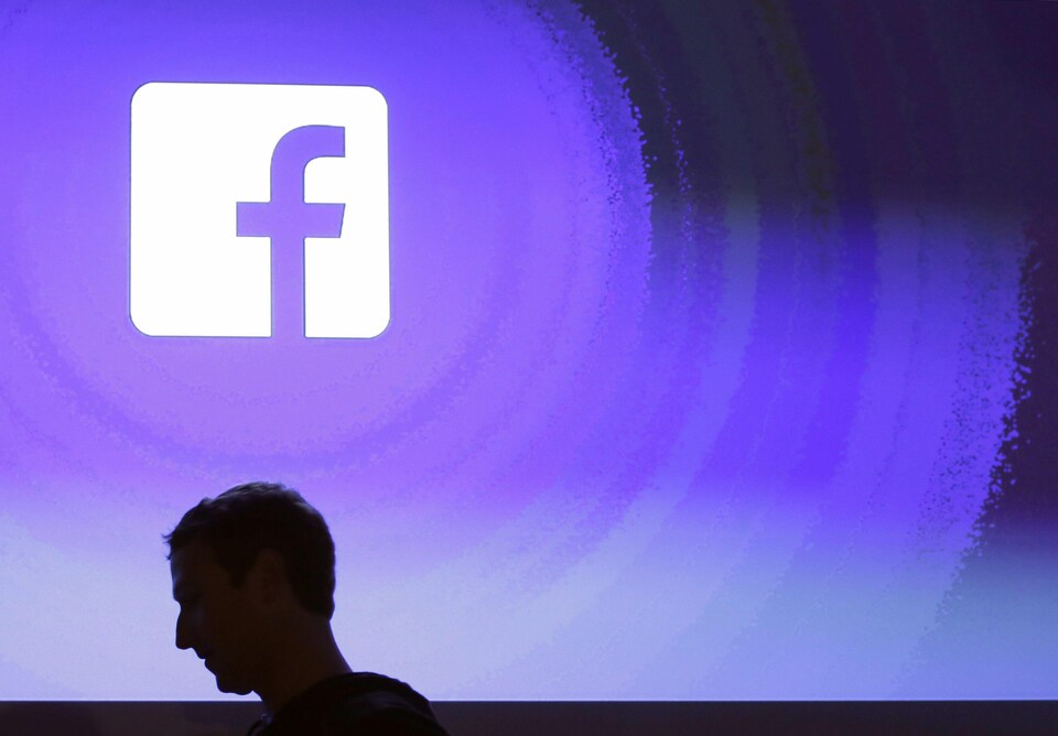 Mark Zuckerberg de profil devant le logo de sa compagnie, Facebook.