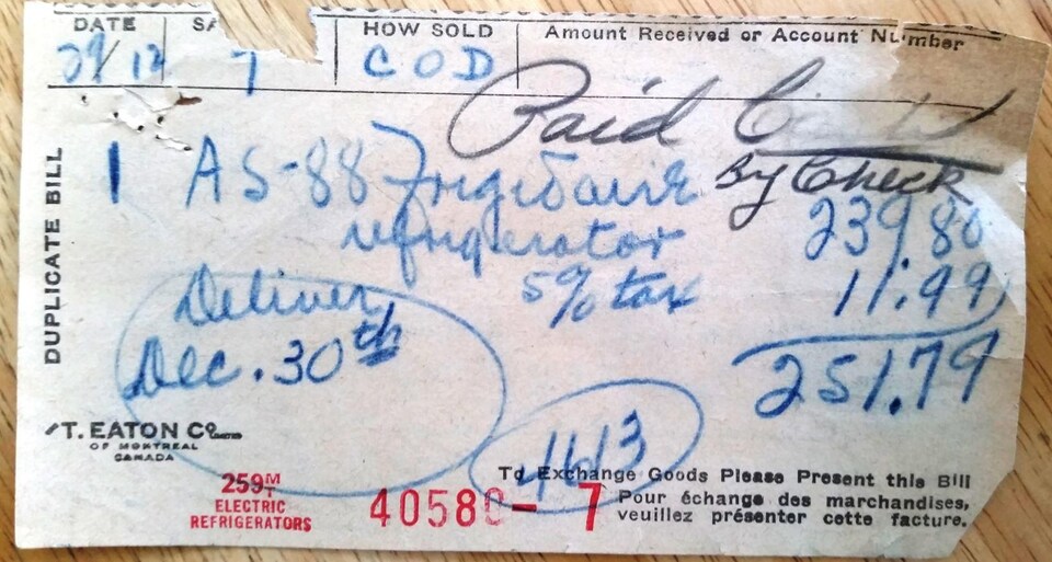 Sur une table en bois, une facture écrite à la main pour l'achat d'un frigo au coût de 271 dollars en 1953.