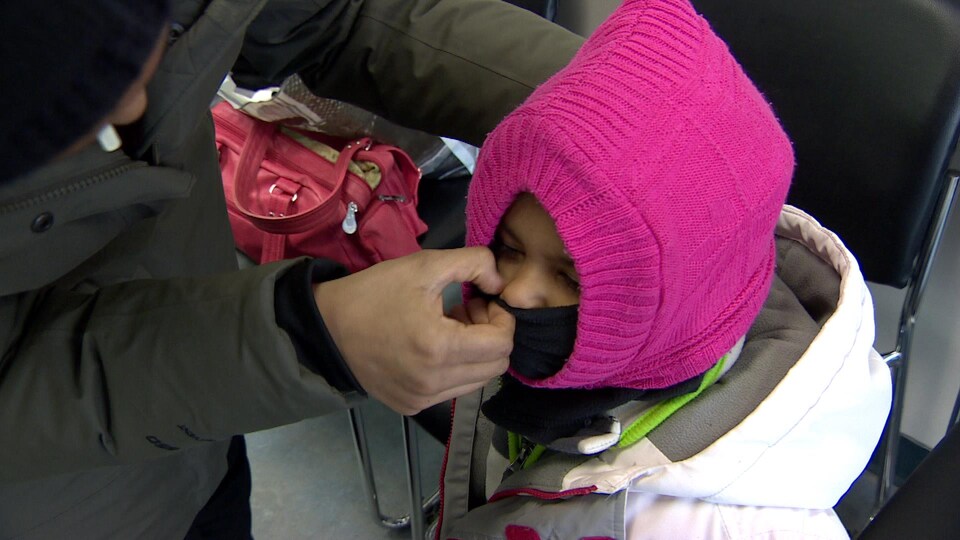 une maman couvre le visage de son enfant couvert par de gros vêtements d'hiver. 