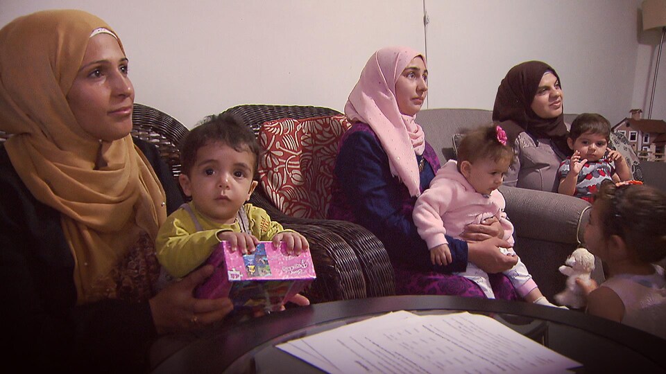 Trois femmes sont assises sur des fauteuils avec leurs petits enfants dans les bras; sur une table au premier plan il y a un papier.