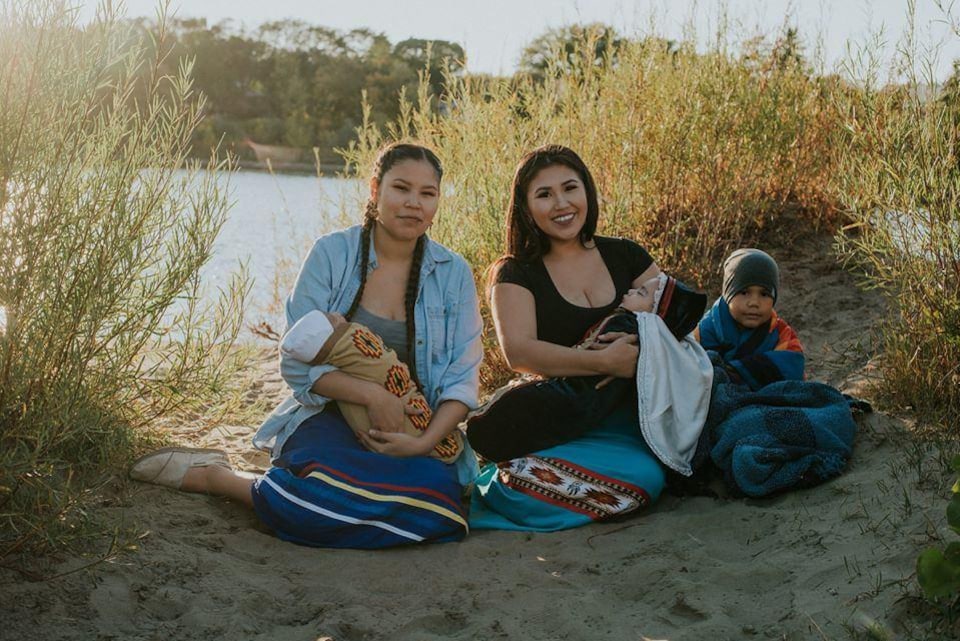 Deux femmes assises dans le sable posant avec leurs enfants.