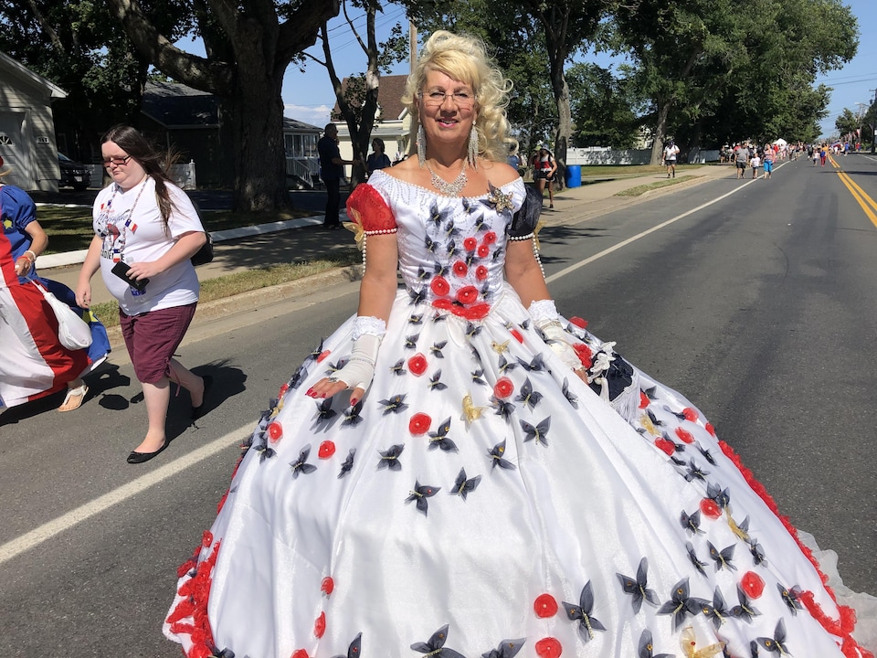 Une femme photographiée dans la rue porte une élégante robe blanche décorée de fleurs rouge et de papillons.