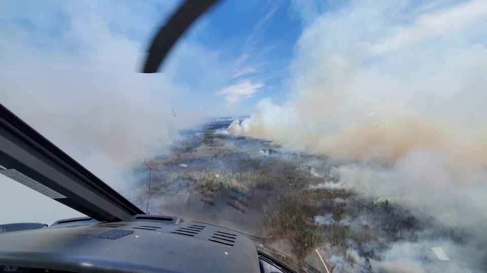 Photo prise d'un hélicoptère qui survole une épaisse colonne de fumée se dégageant d'un feu de forêt.