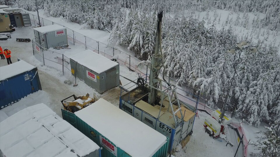 On voit en plongée la machinerie qui sert à forer. Tout autour, la forêt de conifères enneigés.
