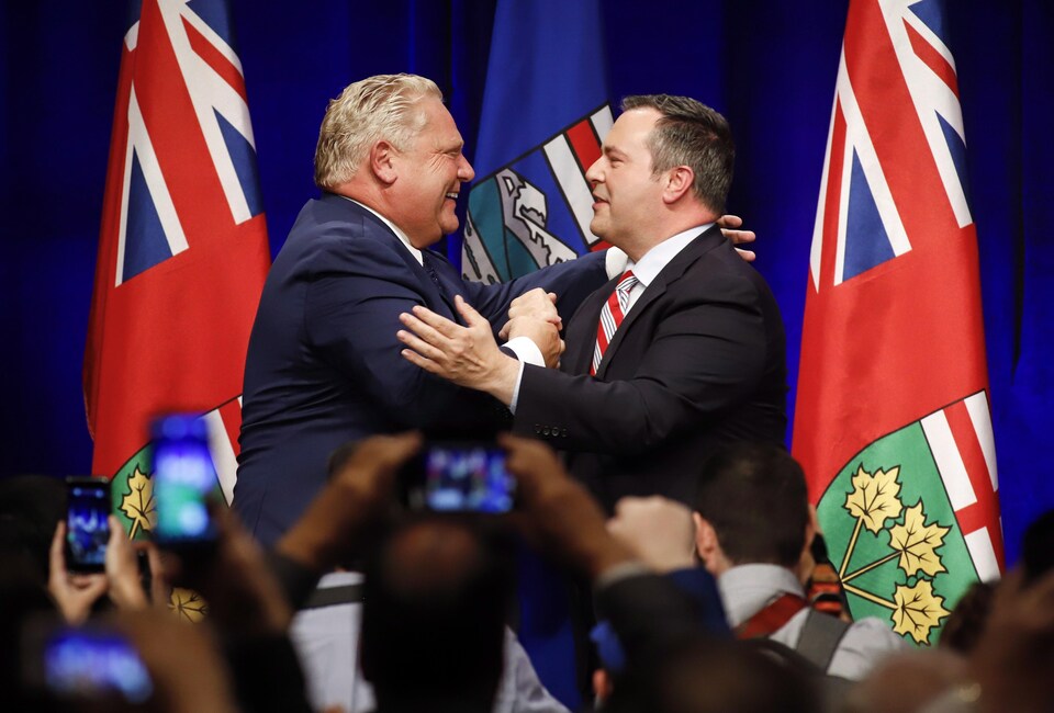 Le premier ministre de l'Ontario, Doug Ford, et le chef du Parti conservateur uni de l'Alberta, Jason Kenney (à droite) se félicitent autour de deux drapeaux lors d'un rassemblement contre la taxe carbone à Calgary.