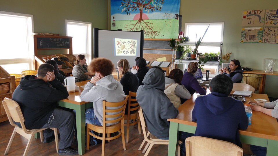 Un groupe d'adolescents écoutent une présentation d'une éducatrice en regardant des images de graines de semence projetés sur un écran. 