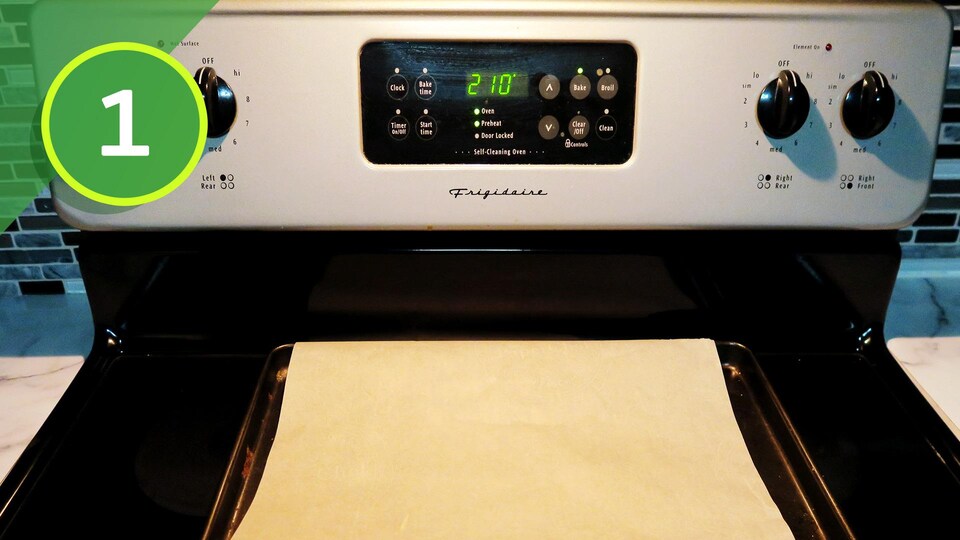 Une plaque de cuisson protégée d'une feuille de papier parchemin sur le dessus d'un four préchauffé à 210 degrés Fahrenheit.