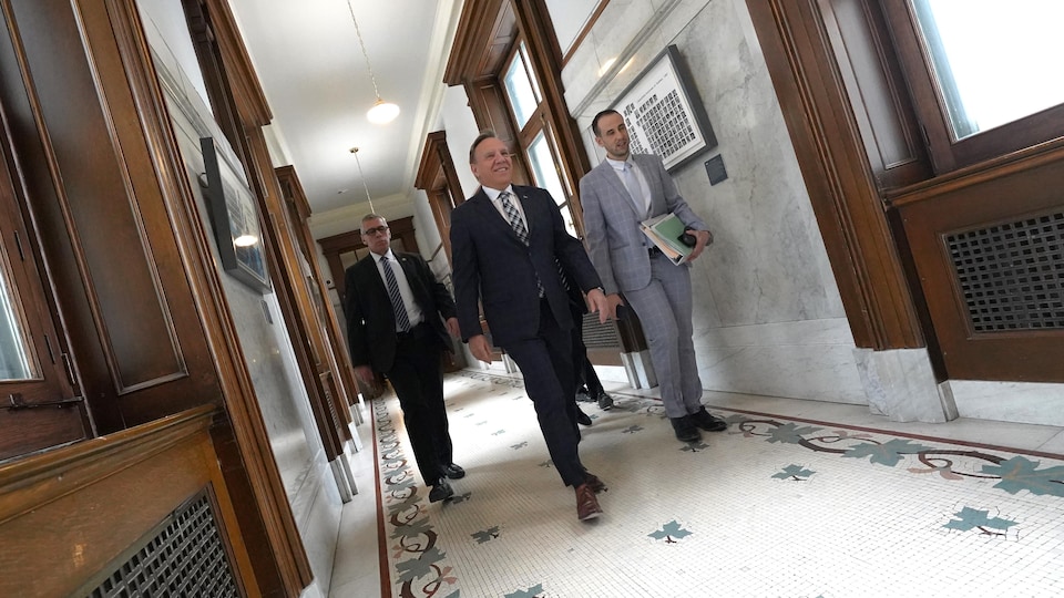 François Legault, accompagné de trois personnes, marche dans les couloirs de l'Assemblée nationale.