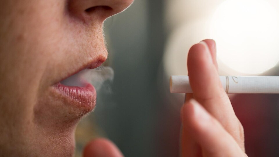 Vue rapprochée de la bouche d'une personne qui fume une cigarette et laisse échapper un peu de fumée