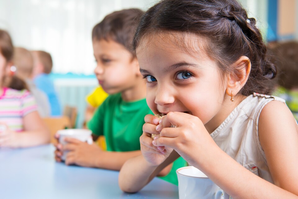 Des enfants assis à une table mangent une collation avec un verre de lait.