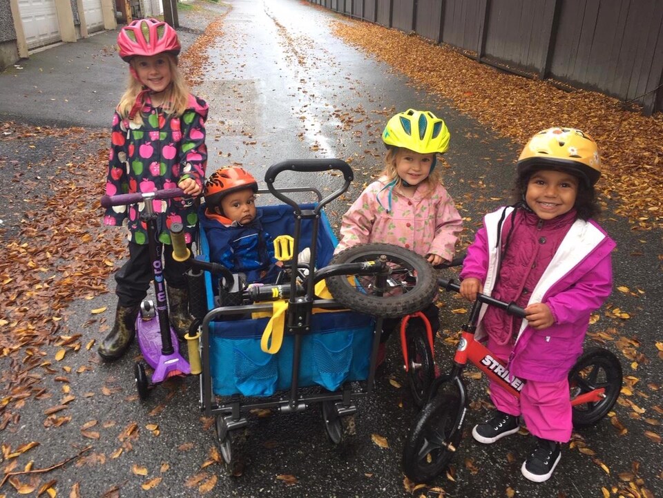 Trois fillettes et un bébé avec des casques de vélos à l'extérieur.