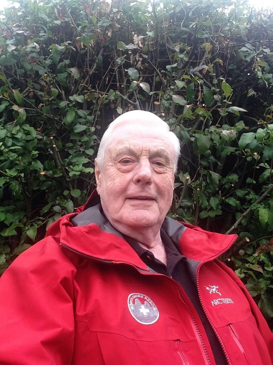 Un homme âgée portant un manteau rouge.