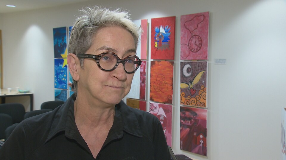 Carmen Gibbs en entrevue devant des peintures qui rappellent le drapeau acadien