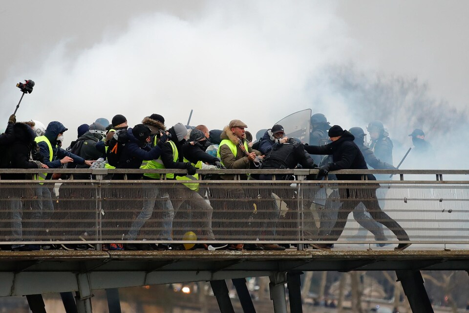 Un homme en noir s'en prend à un policier vêtu d'une tenue antiémeute lors d'affrontements à Paris, en France.