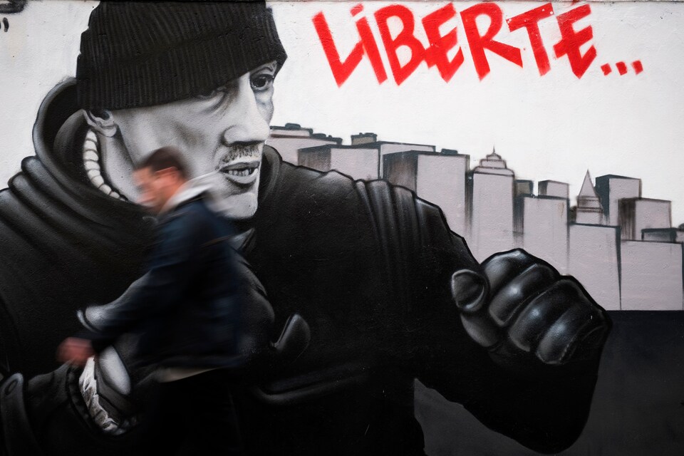 Un homme passe rapidement devant une murale représentant l'ancien boxeur français Christophe Dettinger dans une rue de Paris.