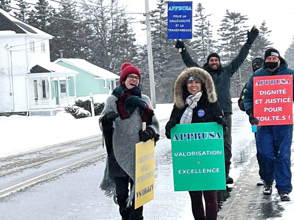 Cinq personnes manifestent sur un chemin rural enneigé avec des pancartes. Elles sont souriantes et lèvent les bras.