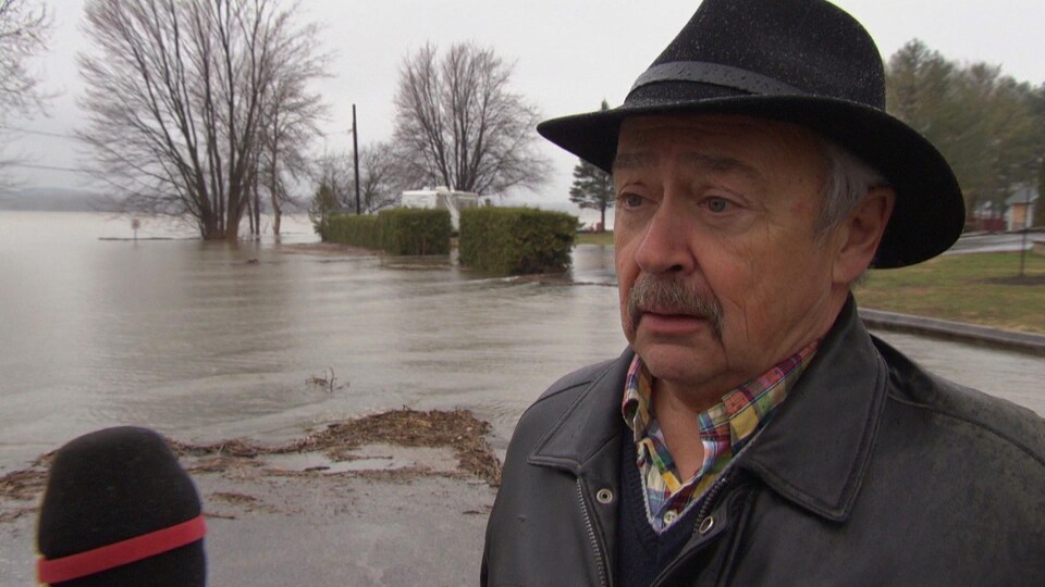 M. Desjardins, coiffé d'un chapeau de feutre, est interviewé sous la pluie, près des berges inondées de Clarence-Rockland.