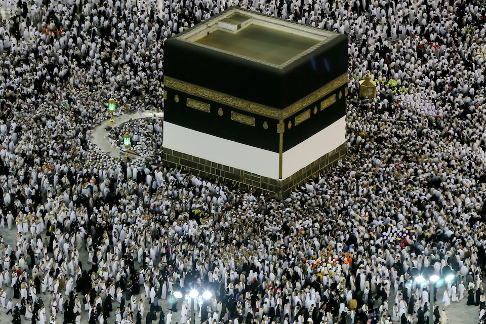 Des musulmans s'agenouillent au pied de la Kaaba, monument cubique noir et blanc de près de 13 mètres de hauteur.