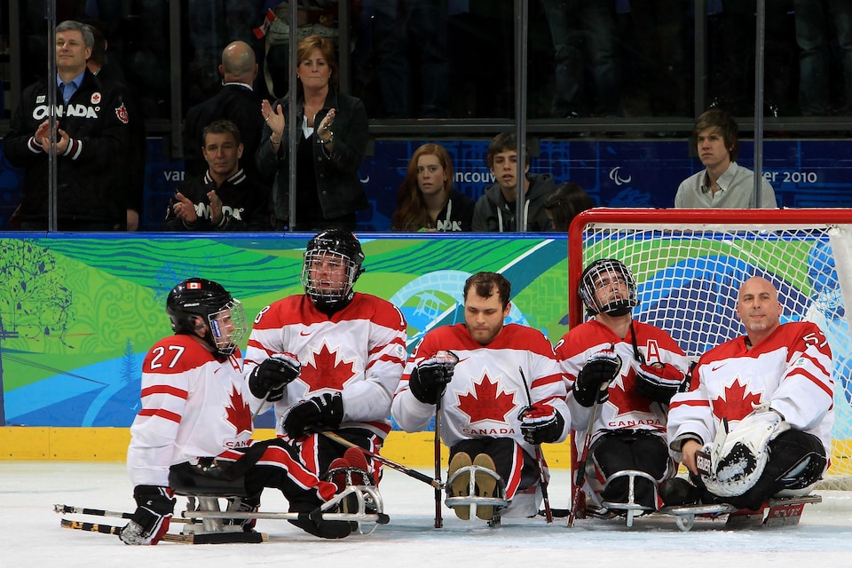 Des joueurs de hockey sur luge. Derrière, le premier ministre canadien de l'époque, Stephen Harper. 