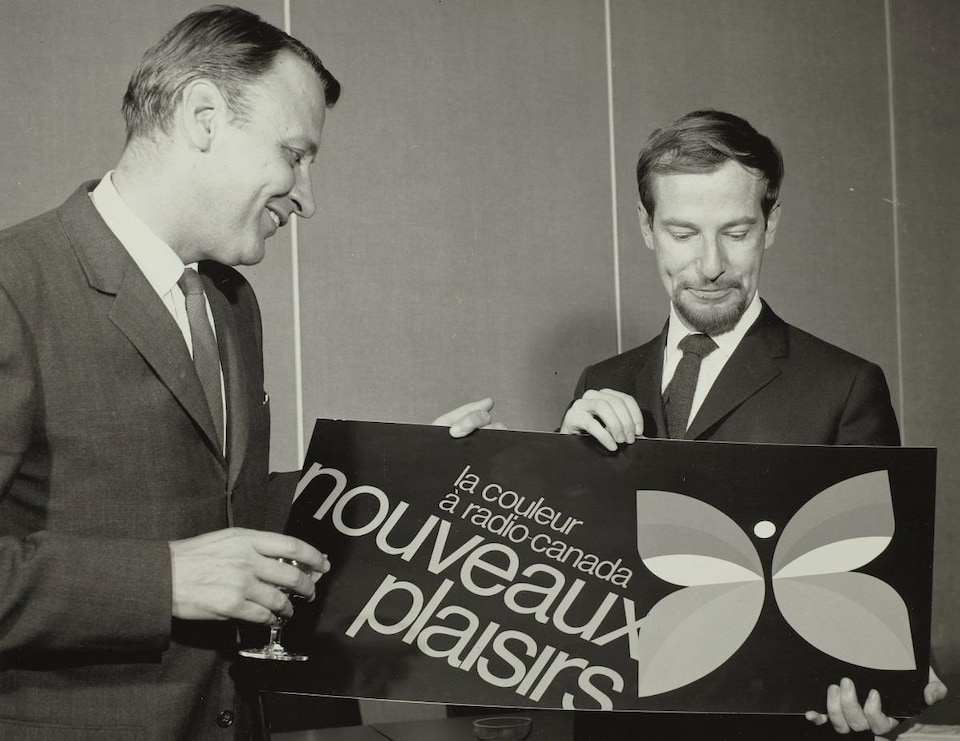 Raymond David, directeur général adjoint de la radiodiffusion française, en compagnie du graphiste Hubert Tison, tenant une affiche montrant le nouveau logo de la Société Radio-Canada, un papillon, symbole de la télévision en couleur.