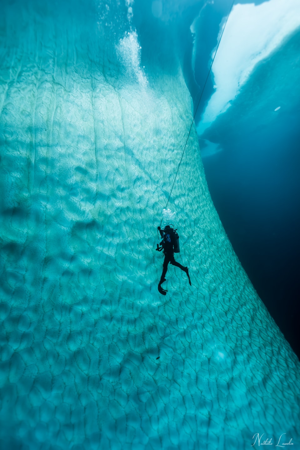 Une plongeuse au plus près d'un iceberg bleuté.