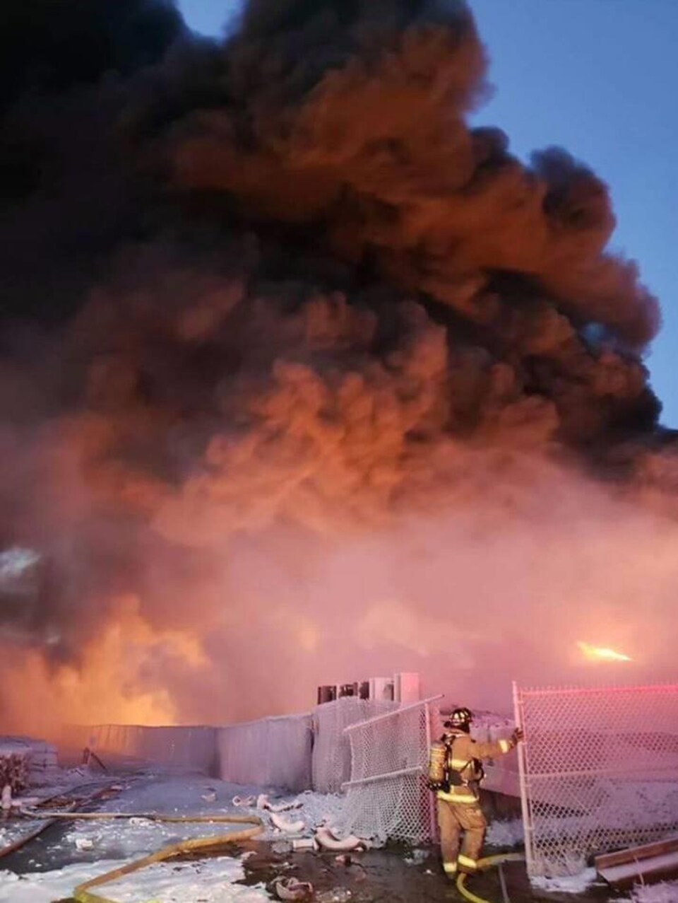 Un pompier près d'une clôture et d'une grande fumée d'incendie de pneus.