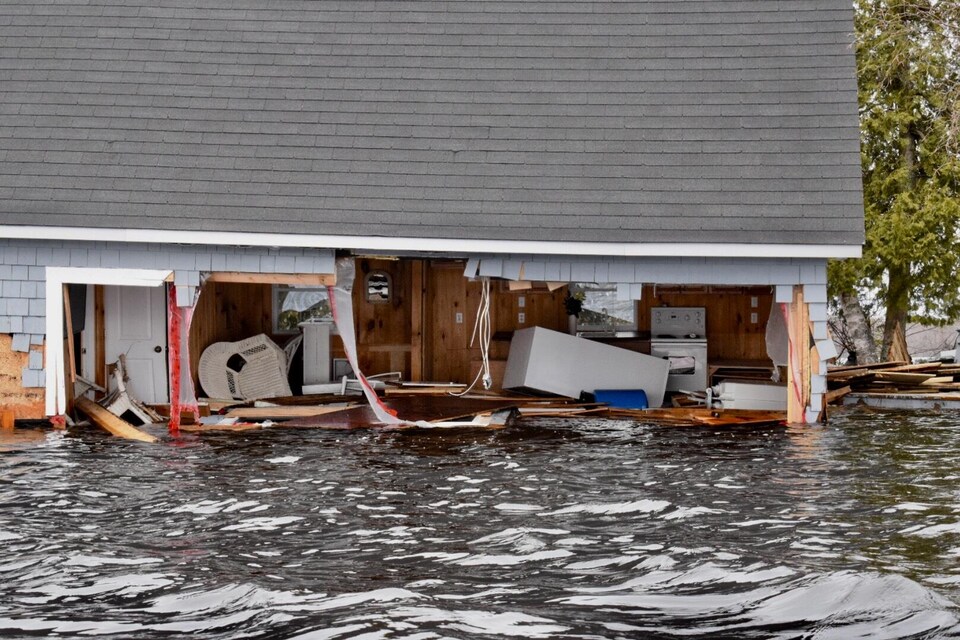 Vue de l'intérieur d'une habitation inondée dont un mur est presque complètement arraché.