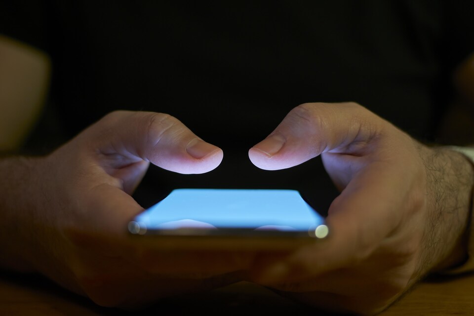 Les mains en gros plan d'un jeune homme qui utilise un téléphone cellulaire.