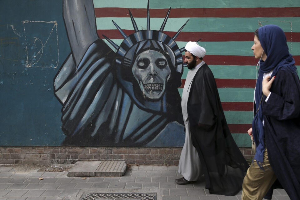 Un religieux chiite et une femme marchent devant une murale caricaturant le statue de la liberté. Le visage de la statue a été remplacé par une tête de mort. . 
