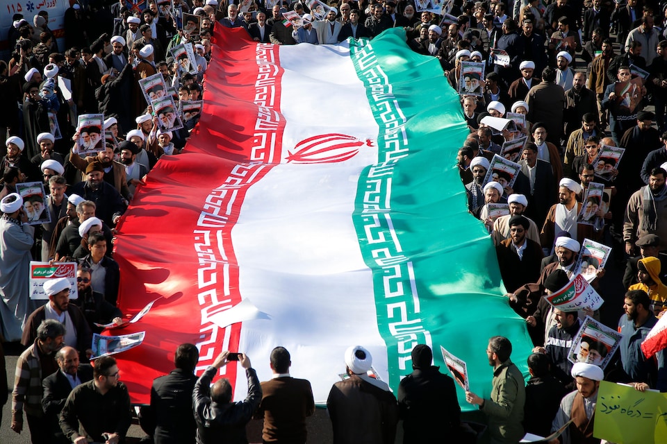 De nombreux Iraniens, dont des mollahs, entourent un drapeau de la République islamique à Qom. 