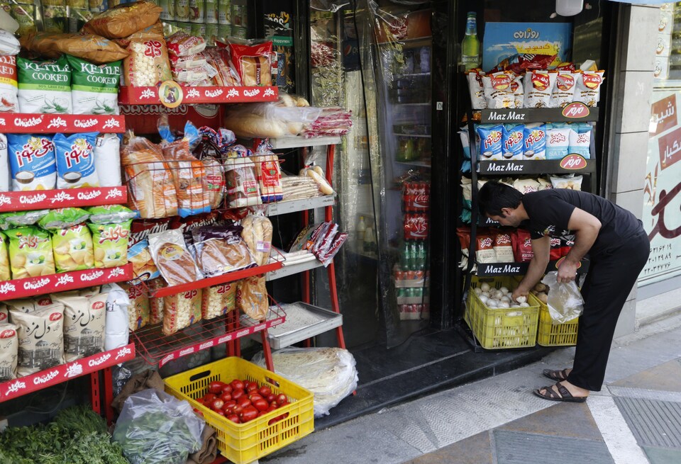 Un homme devant les étalages d'un marché met des denrées dans un sac .