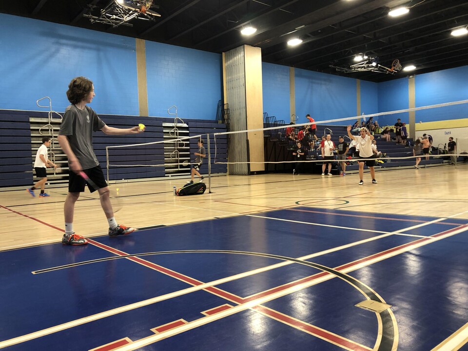 Un adolescent dans un gymnase s'apprête à servir pendant un match de badminton.
