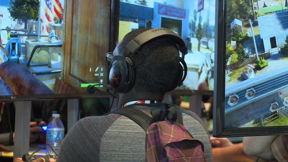Un homme de dos avec un casque d'écoute devant un écran joue au jeu Far Cry 5.