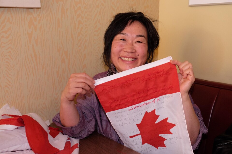 Une femme tient un drapeau canadien sur lequel elle a brodé des mots. 