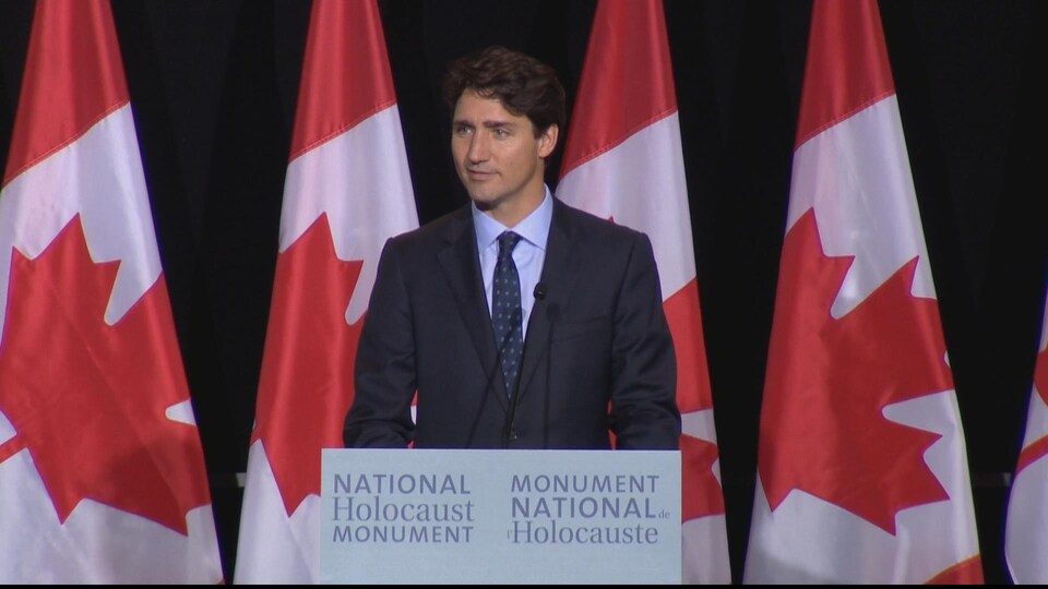 Le premier ministre Justin Trudeau devant des drapeaux canadiens lors de la cérémonie