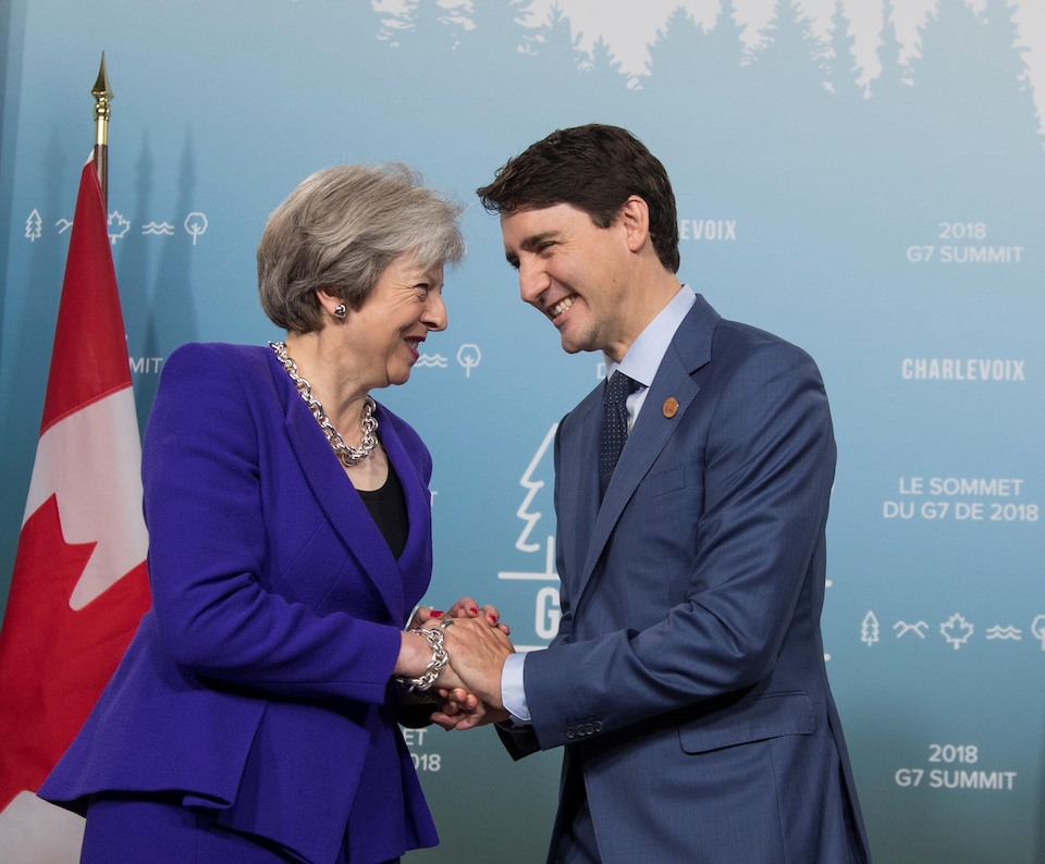 M. Trudeau et Mme May se serrent la main en souriant. 