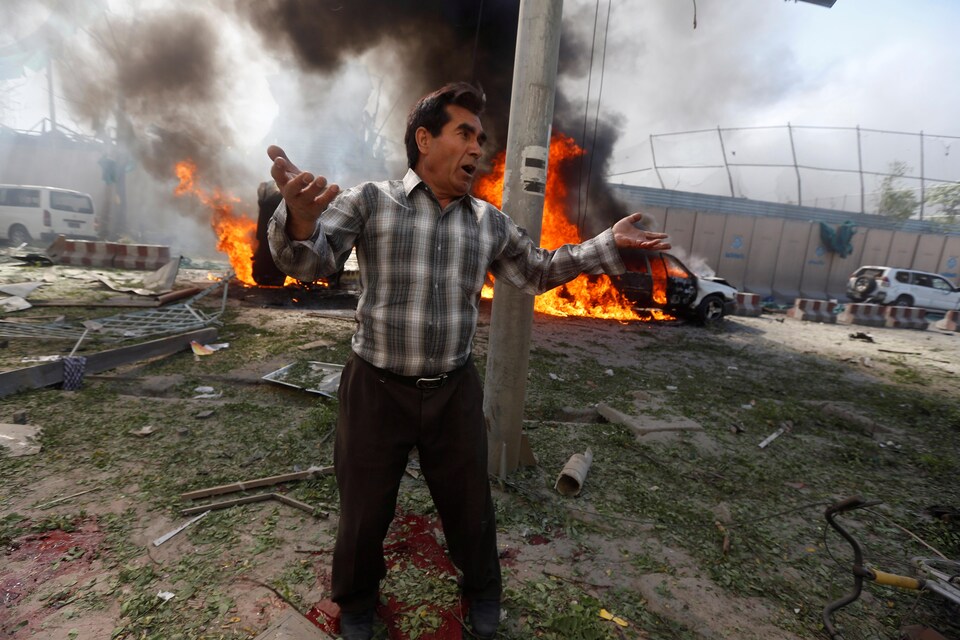 Un homme se trouve sur les lieux de l'attentat à Kaboul, plusieurs voitures brûlent derrière lui.