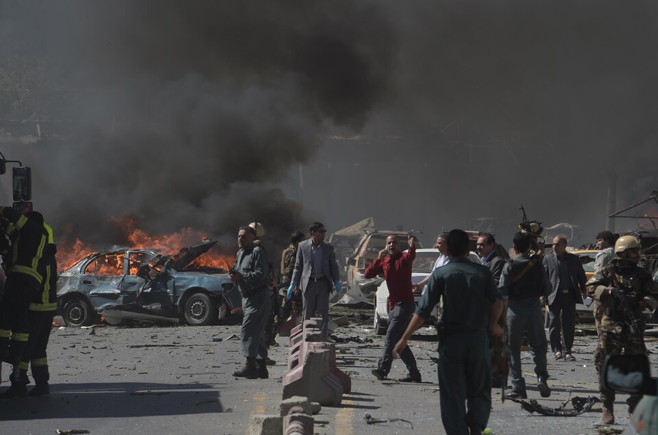 Plusieurs personnes dont des militaires et des secouristes sont sur les lieux de l'attentat, où une voiture en flamme laisse échapper beaucoup de fumée.