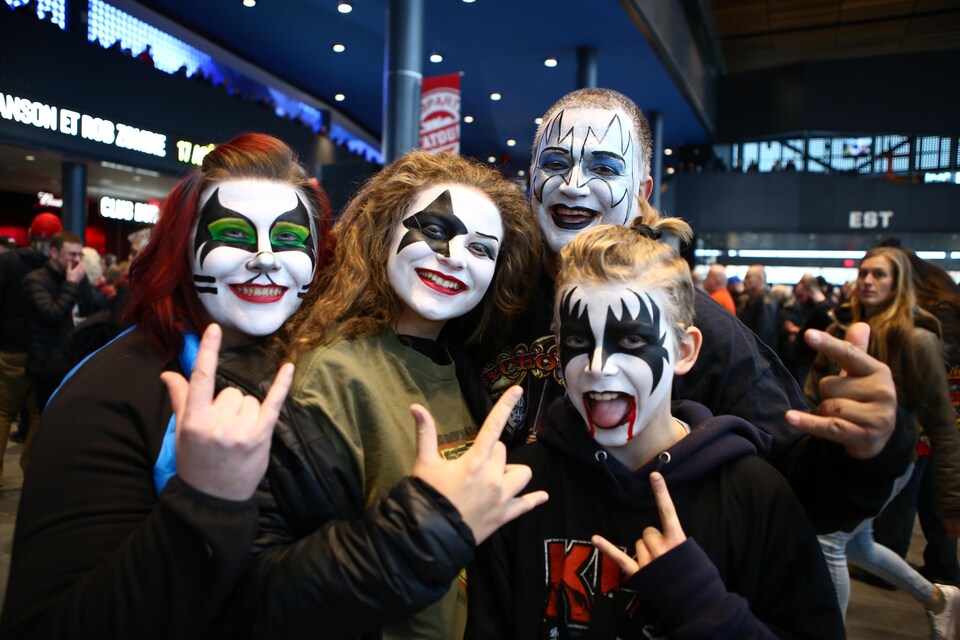 Quatre jeunes adeptes du groupe Kiss qui arborent des maquillages du groupe au visage.